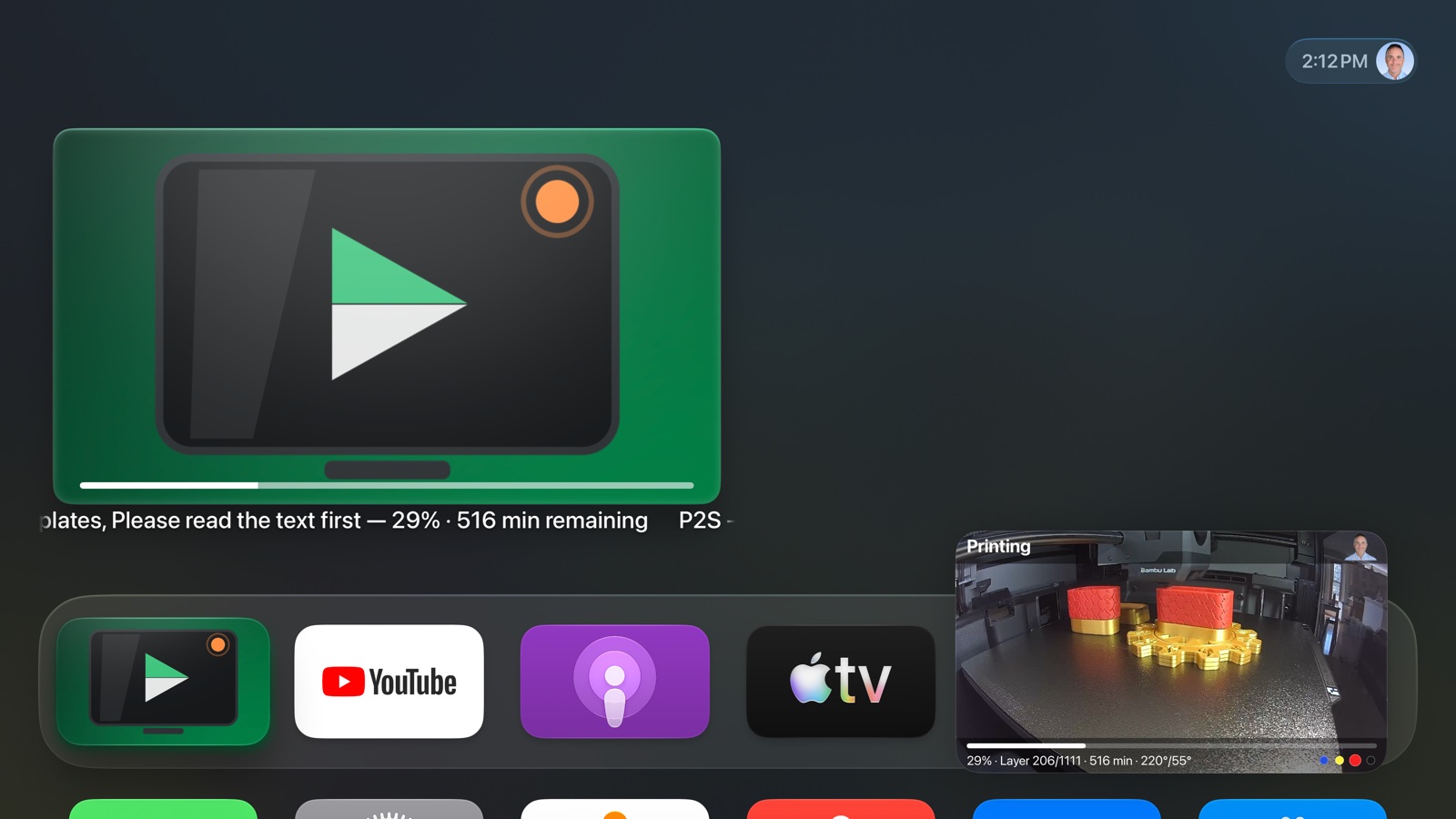 The tvOS Home Screen with AmbientCast on the top shelf showing the print at 29 percent, and the printer's camera feed playing in a Picture in Picture window in the bottom corner.
